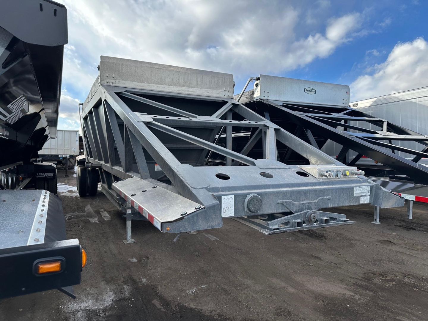 Bottom dump trailer in a yard showing structural frame and front hitch area, with other trailers in background