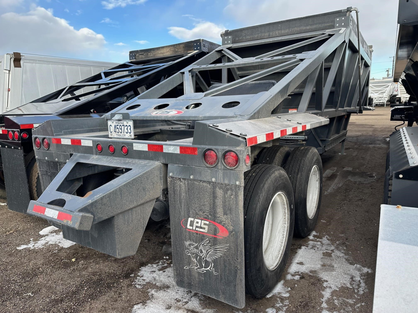 Bottom dump trailer in-metal frame viewed from rear-left side showing CPS logo, dual rear axles, hydraulic hoist, and reflective safety stripes.