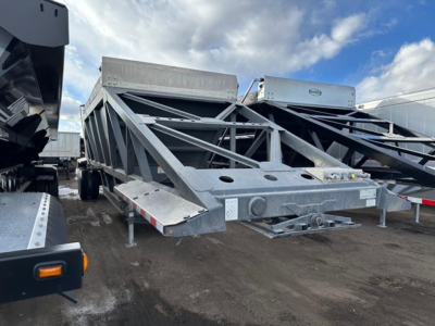 Dump trailer showing bottom-dump frame and coupler with metal frame and safety chains.