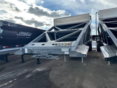 Bottom dump trailer in a storage lot showing the front frame and hydraulic system, with other trailers nearby.