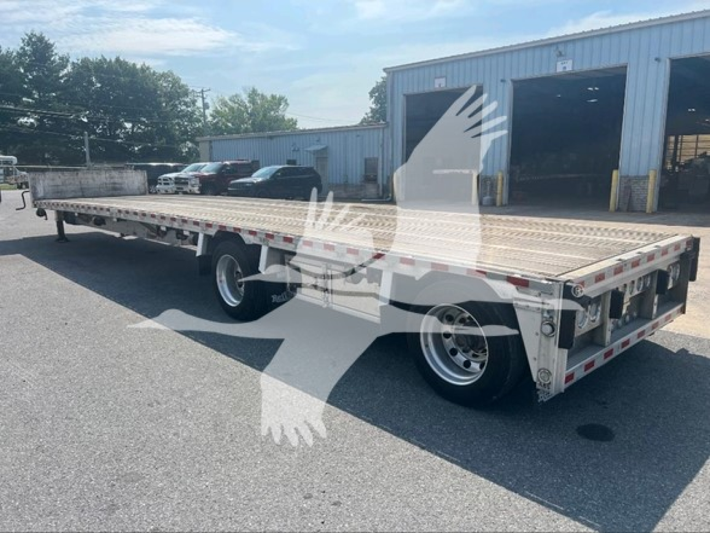 Flatbed trailer showing long dropdeck with dual rear axles and aluminum decking. Side rails and ramps visible; company watermark on image.