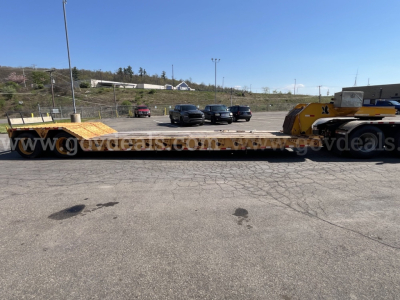 Lowboy trailer long flatbed showing yellow head unit and multiple axles with ramps, side rails, and loading deck.