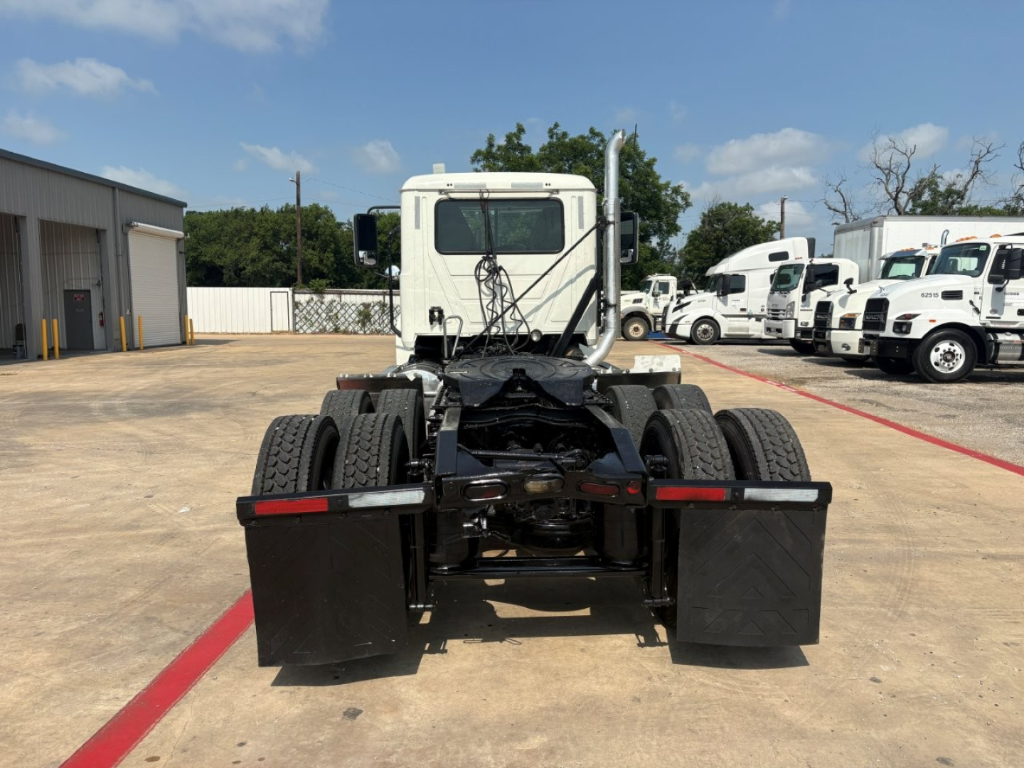 Tractor truck chassis rear view showing dual rear axles and fuel tanks with fifth wheel in the middle. Cab visible in background.