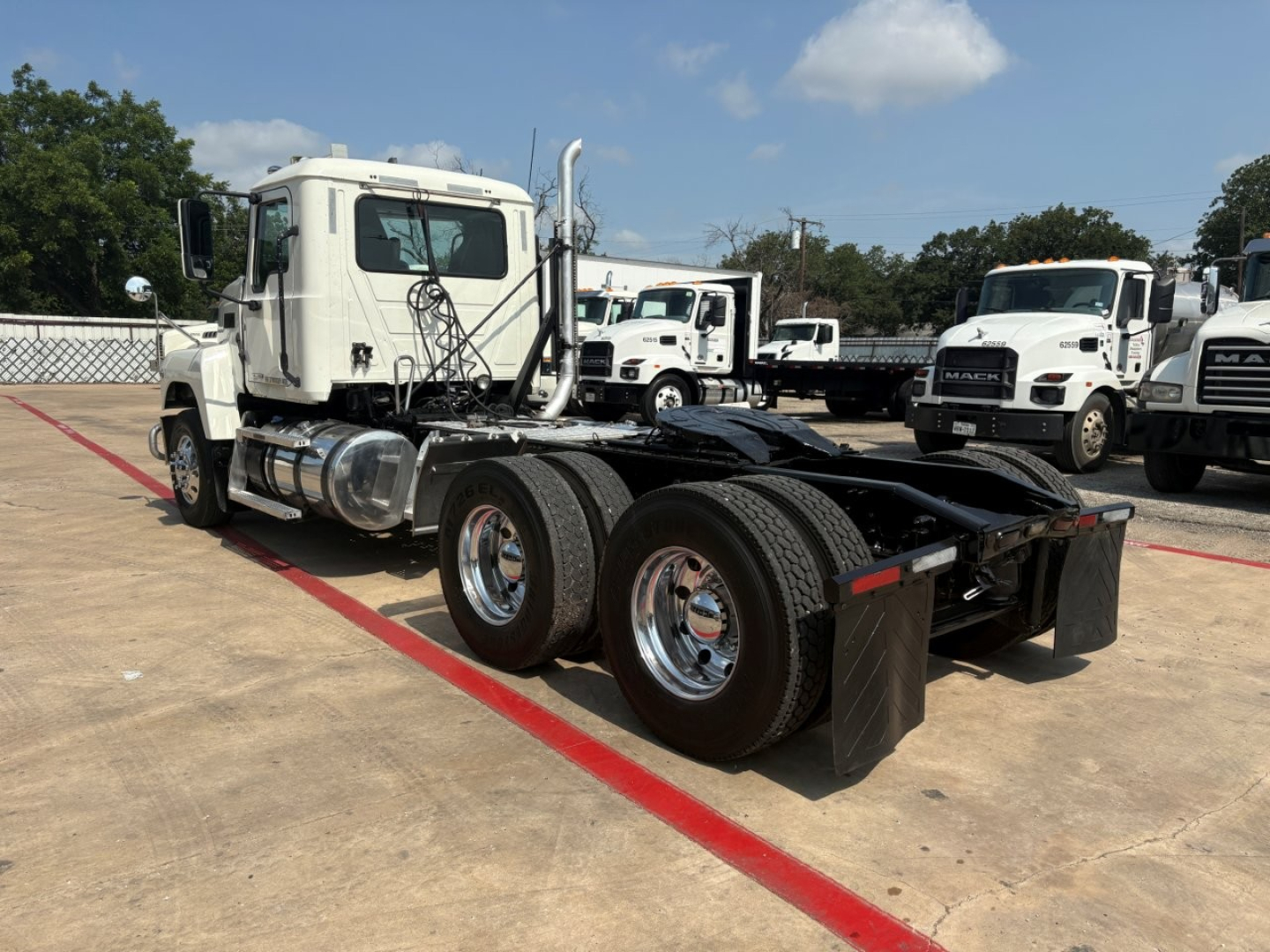 Truck chassis and cab of a 2020 Mack PI64T conventional daycab with dual rear axles and fifth-wheel setup, front view showing white cab and parked trucks.