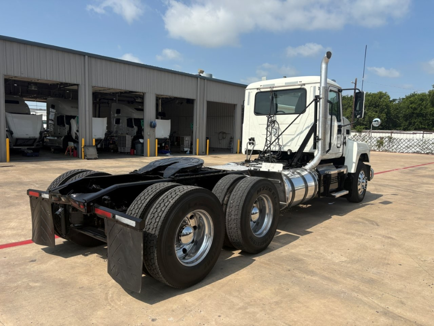 Truck chassis showing rear view of 2020 Mack PI64T with dual rear axles and fifth wheel, white cab, parked in lot.