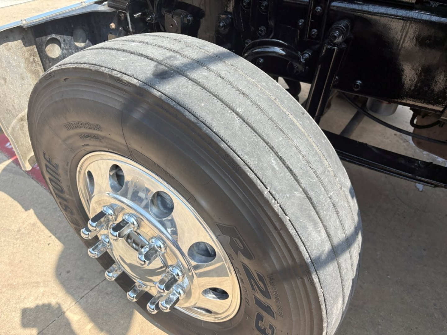 Mack PI64T front wheel showing dual tires and chrome hub with lug nuts, undercarriage and suspension components visible.