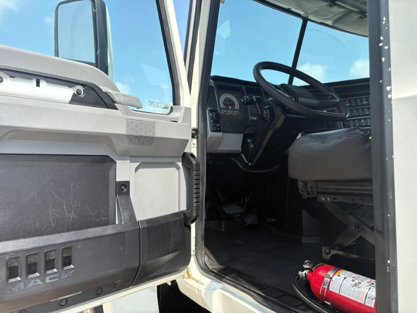 Mack PI64T truck interior cabin view through open door showing steering wheel and dashboard.