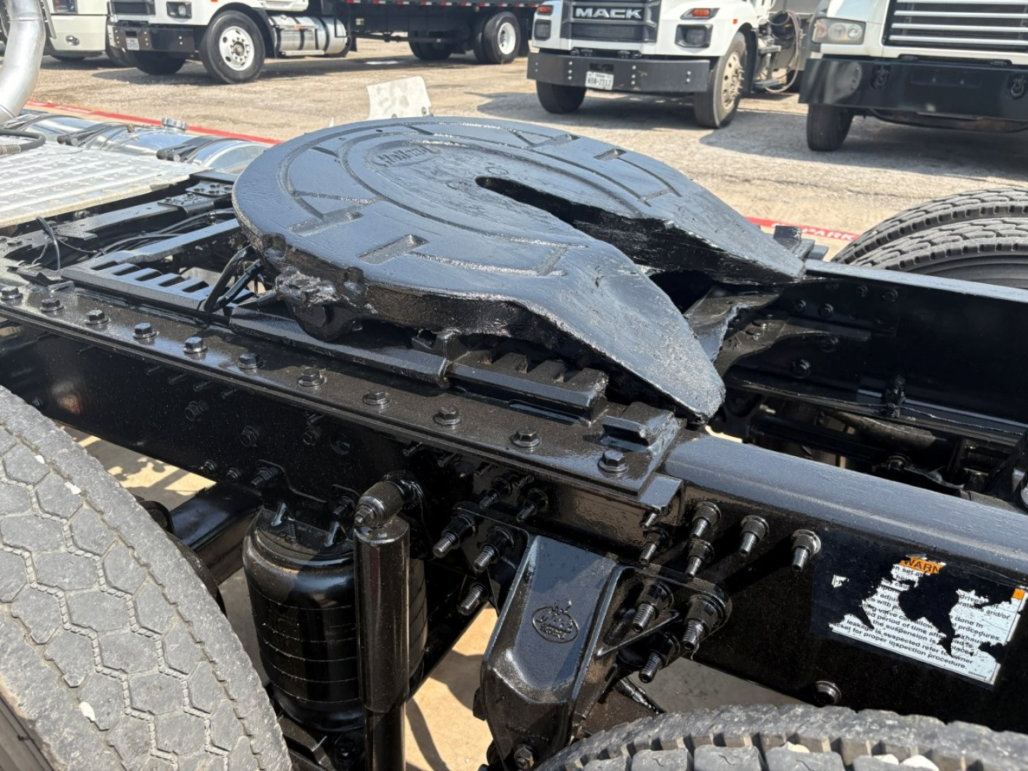 Truck chassis showing fifth wheel and mounting hardware on a Mack PI64T daycab with hydraulic air suspensions and frame rails.