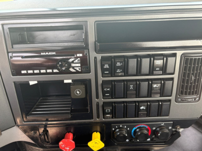 Mack PI64T truck dashboard showing stereo head unit and numerous switches and climate controls with red and yellow power knobs.