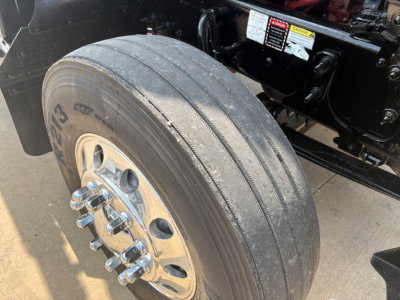 Mack PI64T front wheel and tire with dual rear axle components visible in a truck bay.