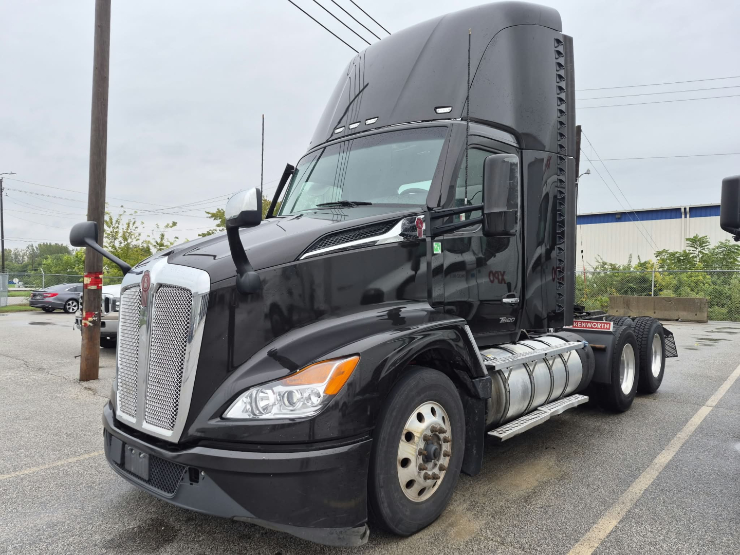 Kenworth T680 conventional daycab tractor from left-front angle, black exterior, large grille, dual fuel tanks, visible OEM badge, side view mirrors.