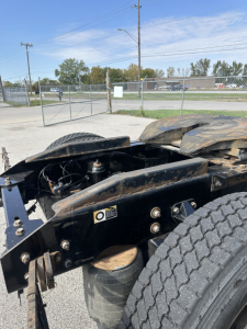 Truck chassis and dual rear wheel area of a 2022 Kenworth T680 in-service condition, showing frame rails, suspension air bags, and labeling near the cab area.