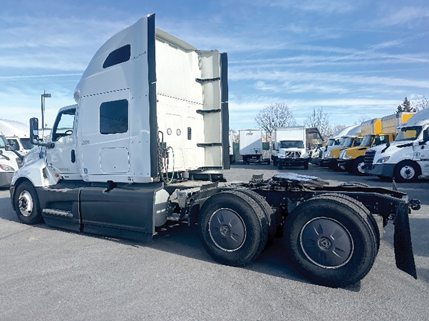 Truck tractor for International LT625 side view showing cab and dual rear axles with fifth wheel area and cargo trailers in background.