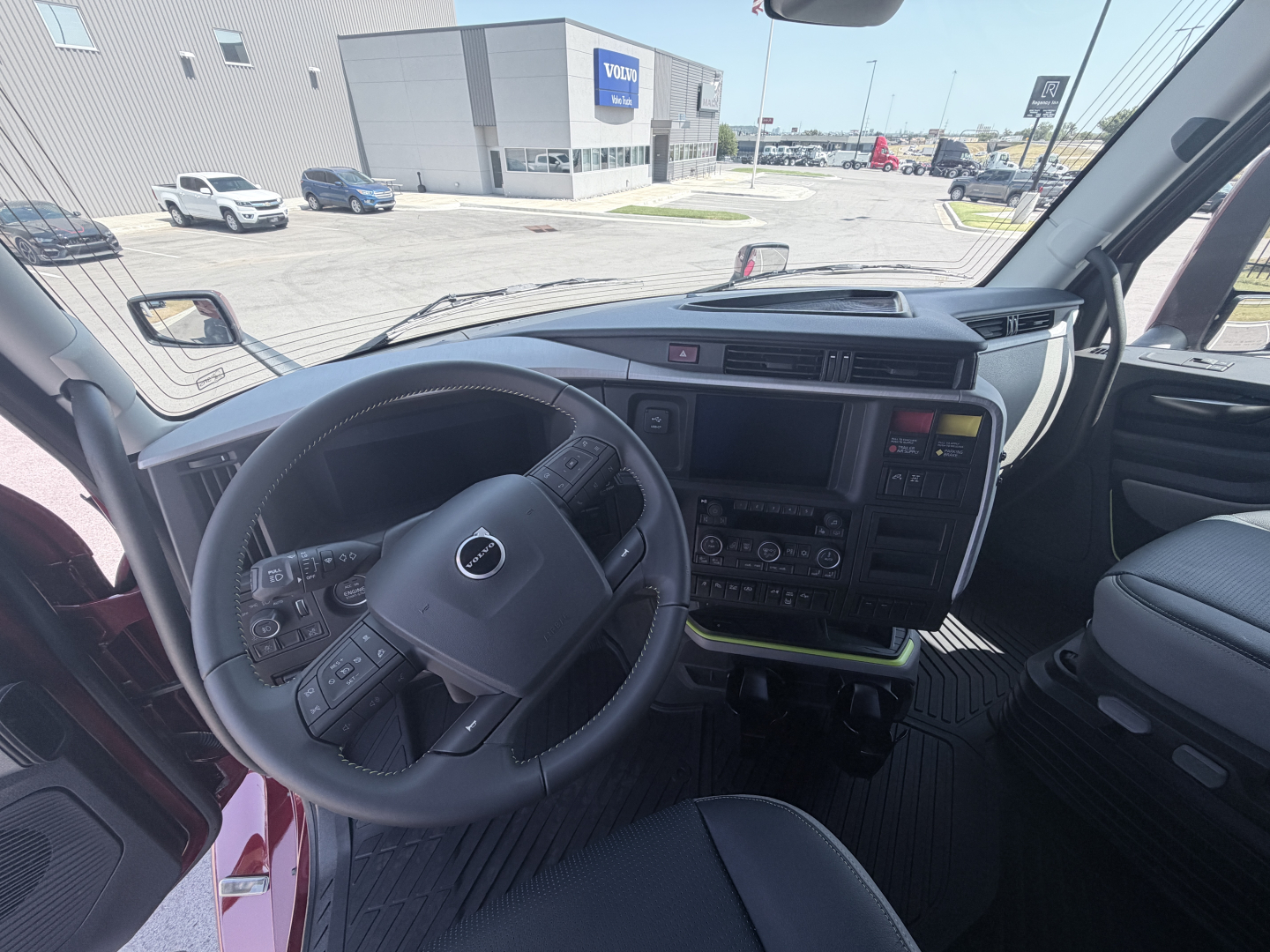Volvo truck cab interior with steering wheel, dashboard, and center touchscreen. Visible on the console: various controls, gear selector, and a hooded instrument cluster.