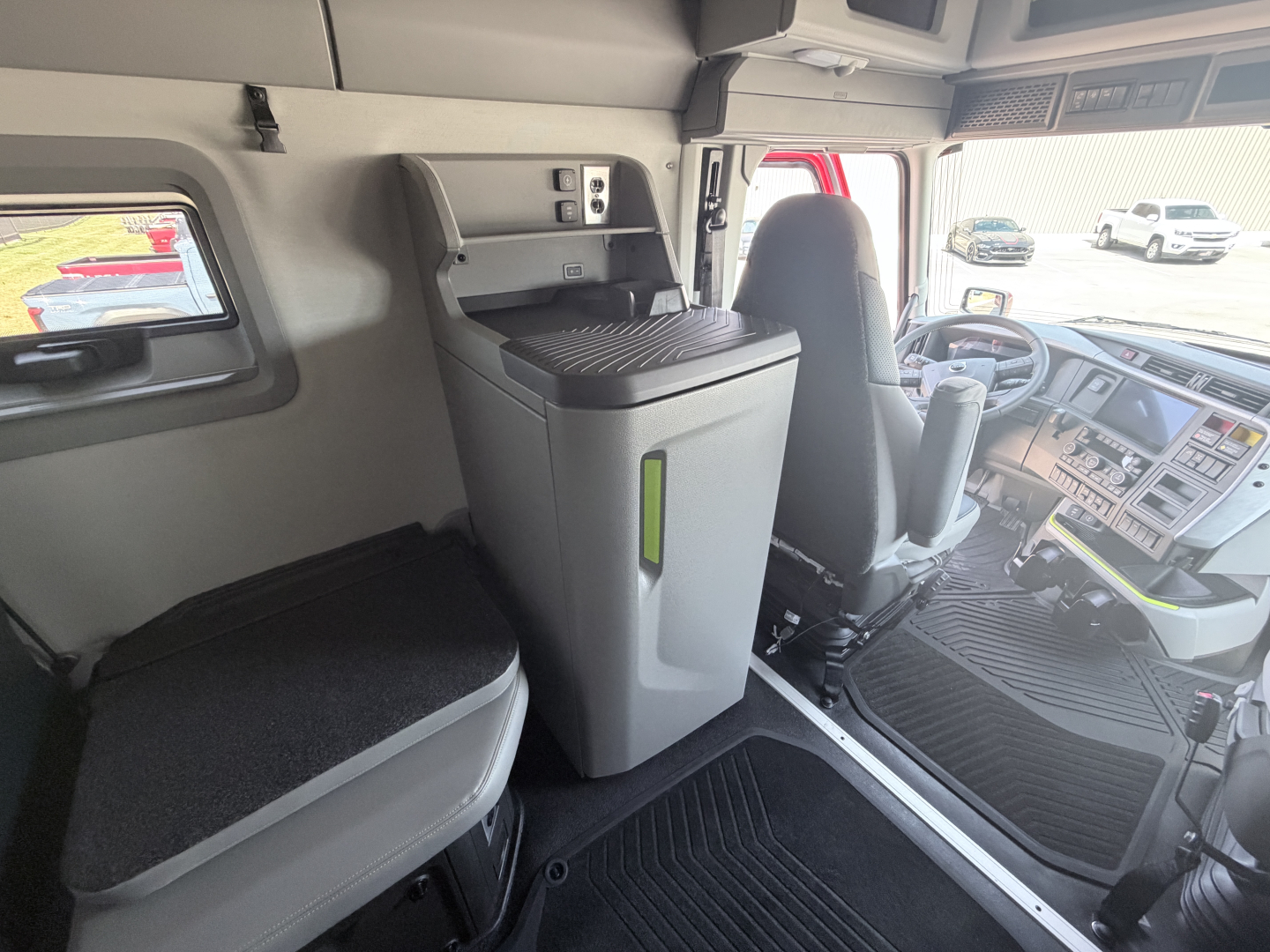 Rear cabin area of a 2027 Volvo VNL64T860 truck showing center console with storage, driver seat, and dashboard/controls visible.