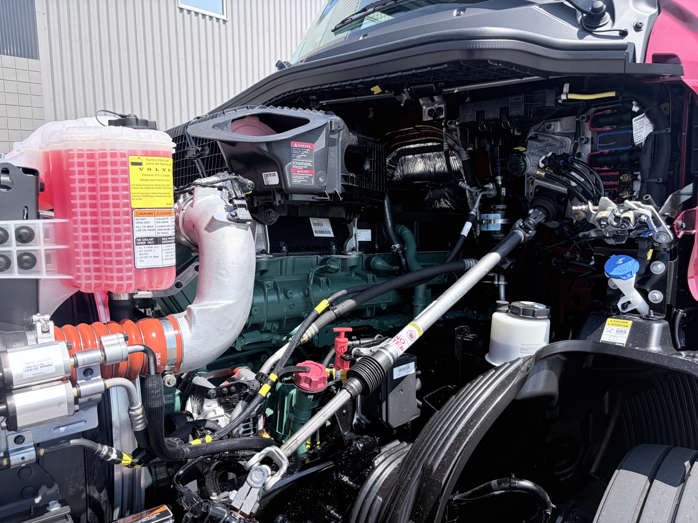 Volvo VNL cab over engine bay showing large coolant reservoir, turbocharged diesel engine, hoses, and various labeled fluid caps.