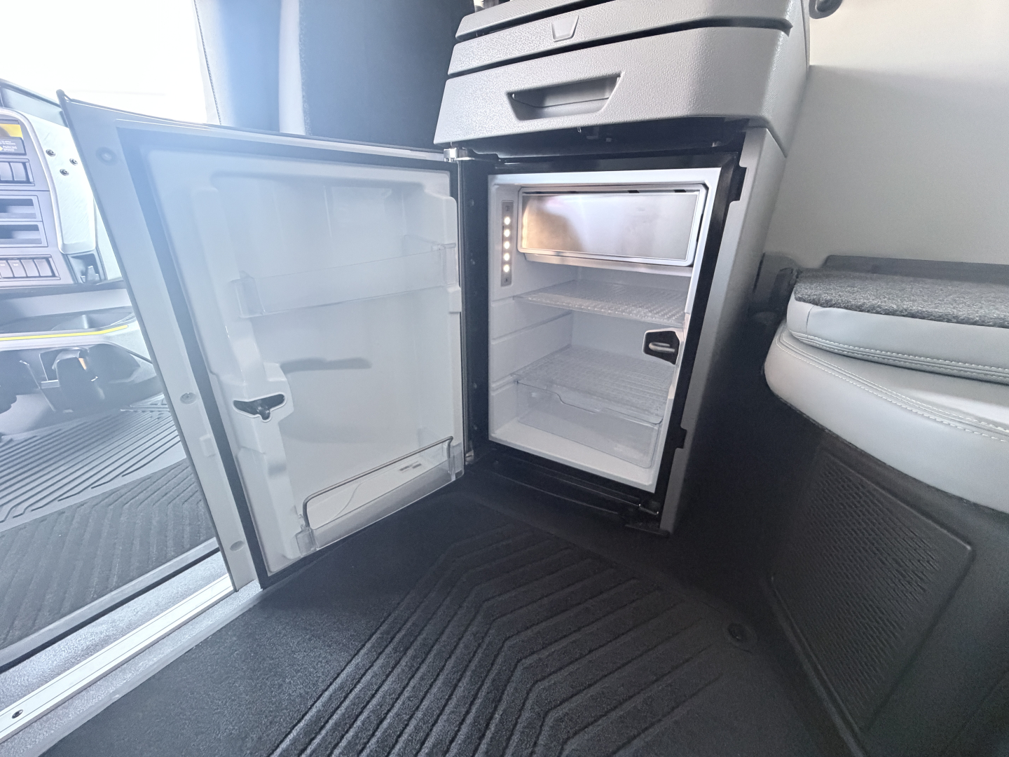 Volvo VNL64T860 sleeper cab interior showing open mini-fridge with empty shelves and freezer, compact kitchenette area.