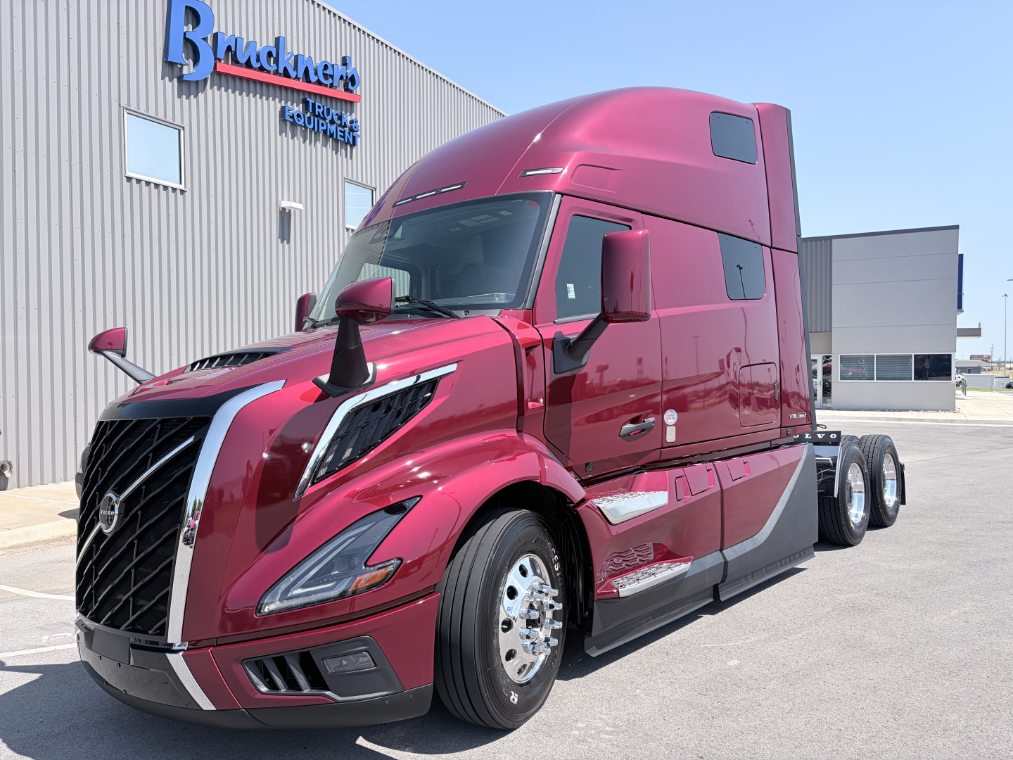 Volvo VNL64T860 truck in magenta color showing semi-trailer tractor with high-roof sleeper and chrome grille in front of dealership.