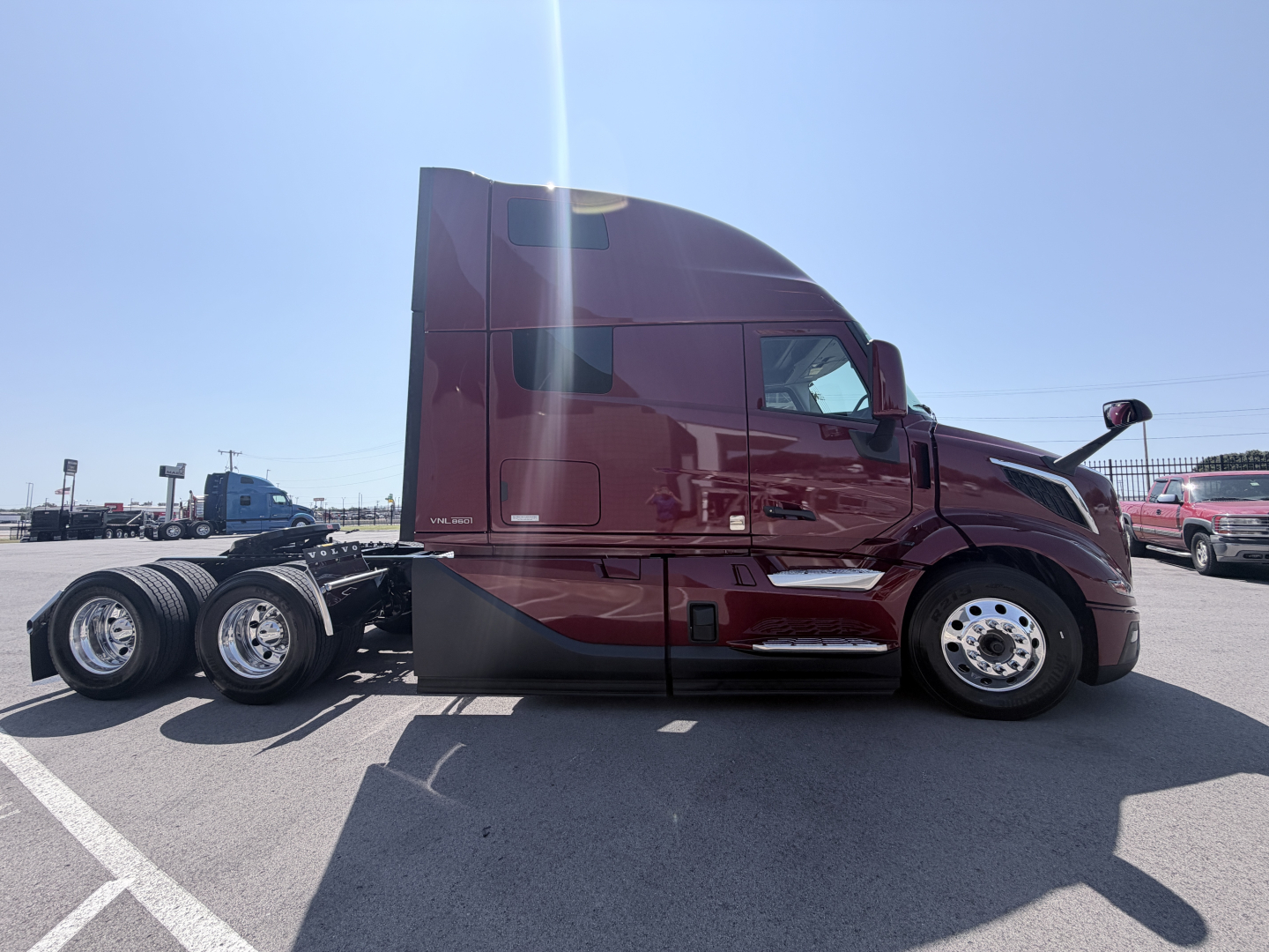 Truck side view showing a maroon Volvo VNL cabin with sleeper, front wheel, and rear dual axles; glossy exterior, chrome wheels, and side mirrors visible.
