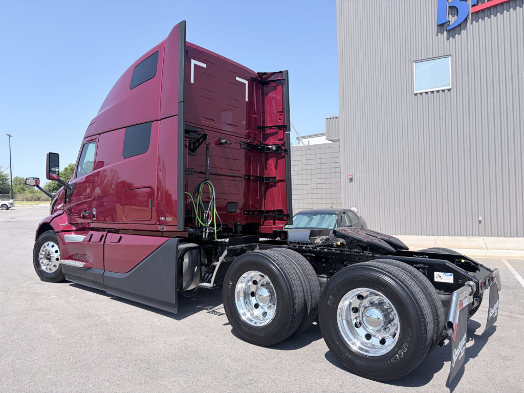 Volvo VNL64T860 tractor cab side view showing sleeper cab and rear wheels with dual rear axles, maroon paint, chrome wheels, and fifth wheel on chassis.