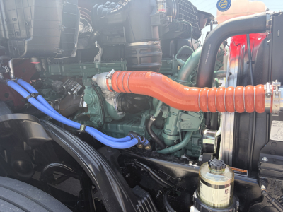 Volvo VNL engine bay showing orange intake hose, green engine block, blue coolant lines, and surrounding components.