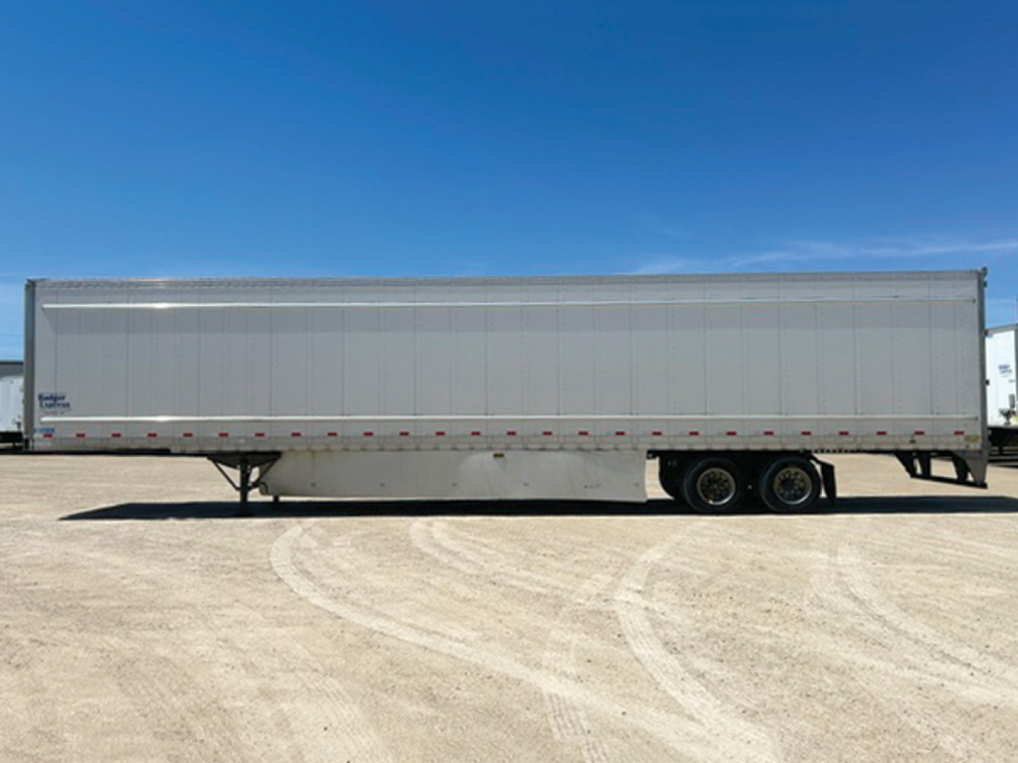 Trailer side view showing a large white Stoughton trailer with tandem axles and smooth metal siding.