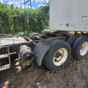 Conventional truck tractor rear wheels and fifth wheel area visible with dual tires and air tanks; Freightliner Cascadia tag may be present in background.