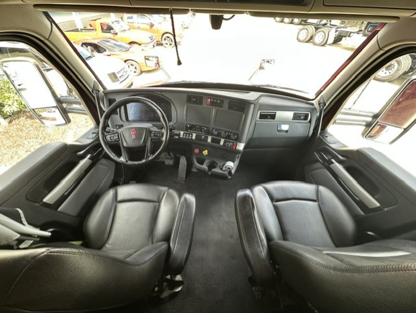 Kenworth T680 cab interior showing steering wheel, dashboard, and two front seats.