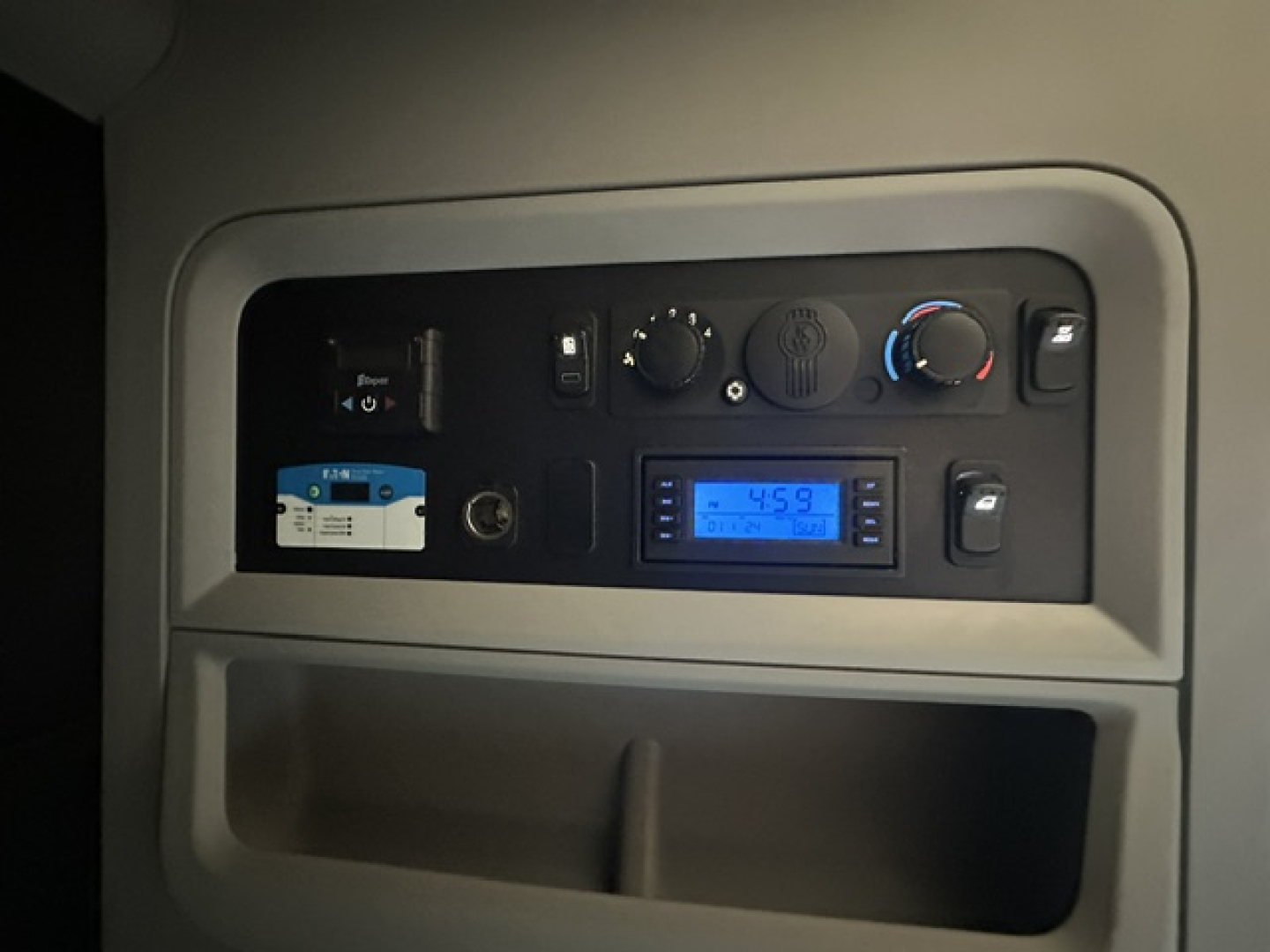 Kenworth T680 cab interior dashboard area showing controls, digital gauge, and vents. Blue-lit display in center console.