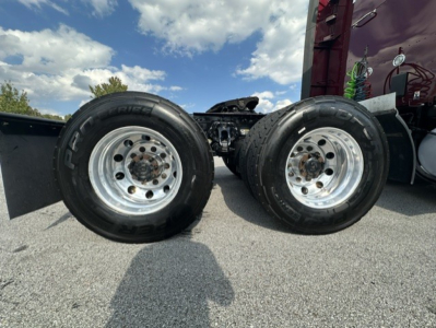 Kenworth T680 rear axle wheels visible with dual tires and chrome rims; part of truck chassis and suspension in background.