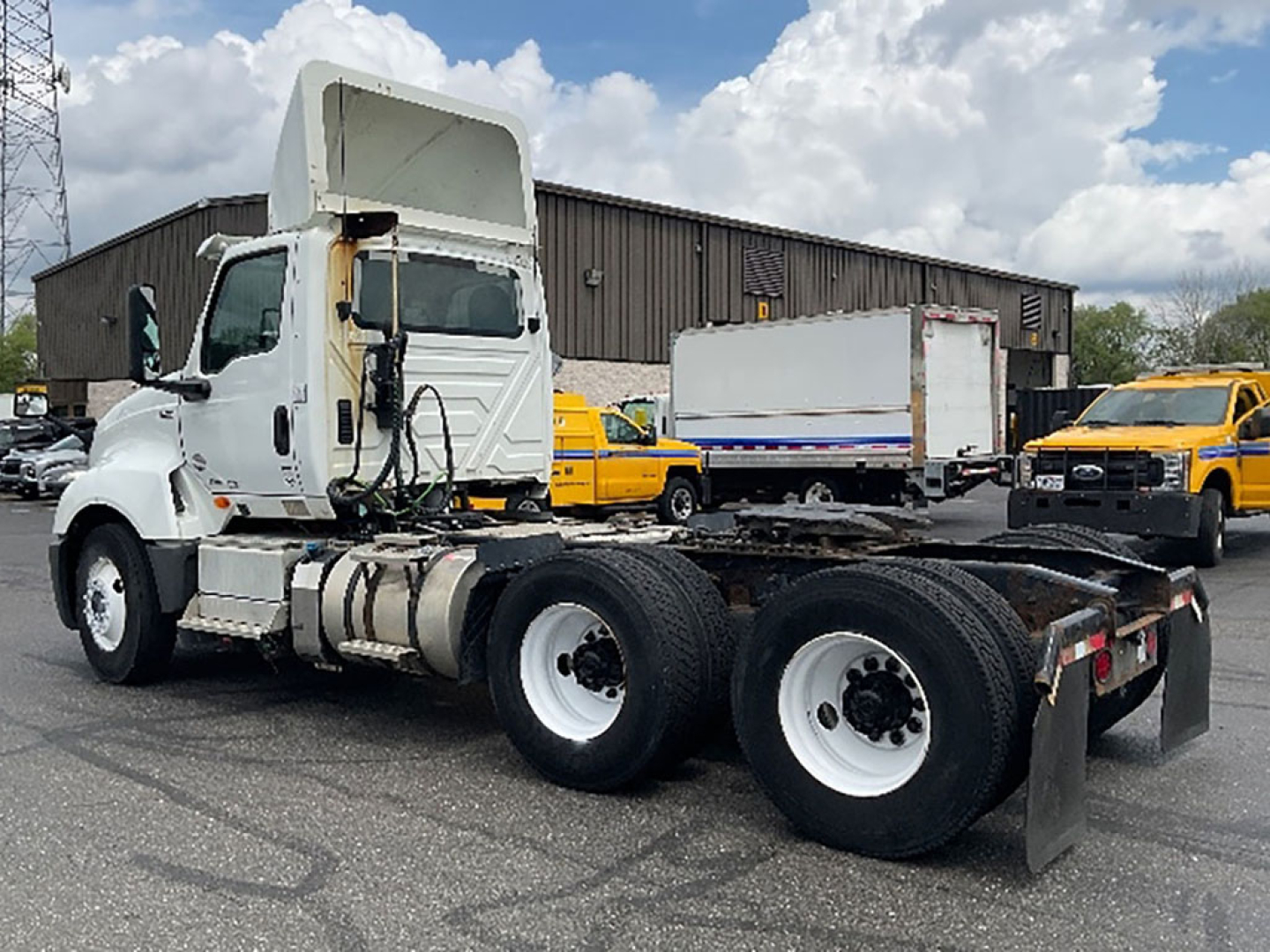 Truck chassis and cab of a 2019 International LT625 in a lot with other yellow trucks in background.