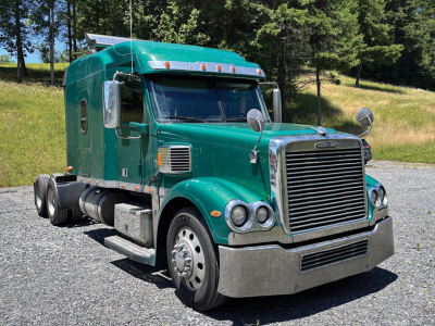 Truck image showing a green Freightliner Coronado cab with chrome grille and dual round headlights, sleeper tractor on a gravel lot.