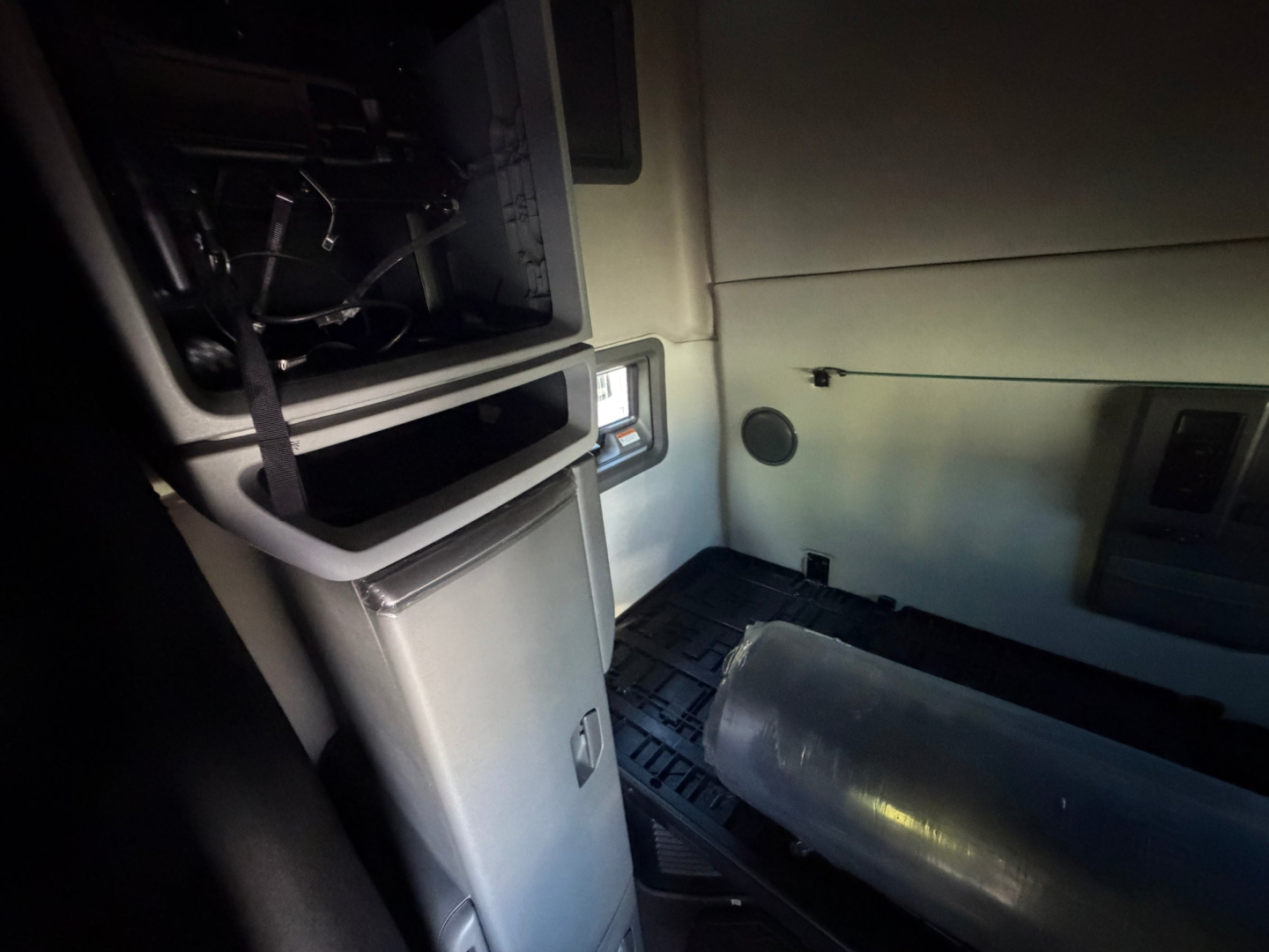 Truck cab interior with exposed wiring and a cylindrical fuel tank or air tank lying on the floor; dashboard area and panels visible.