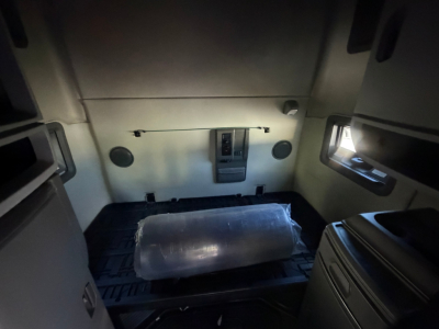 Truck sleeper cab interior showing cargo area with protective plastic-wrapped item and side window, Volvo VNL64T760