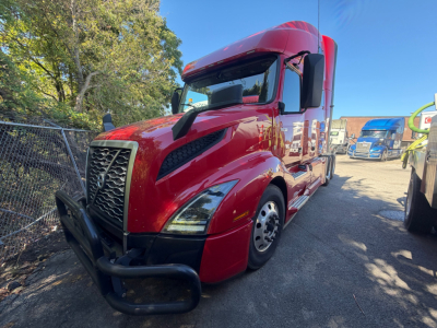 Volvo VNL64T760 sleeper tractor in red with black front bumper and large grille, side view, parked on lot.