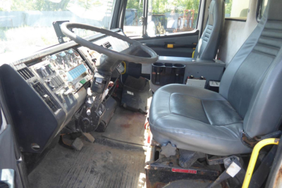 Interior cab view of a 1999 Freightliner FL70 with two seats, steering wheel, dashboard, and plow truck controls.