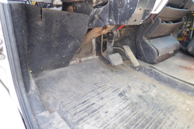 Freightliner FL70 cab interior showing floor area and foot pedals with dirt and rubber mat.