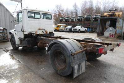 Truck chassis of a Freightliner FL70 with cab and rear frame exposed, showing rusty drive components and dual rear wheels without a cargo bed.