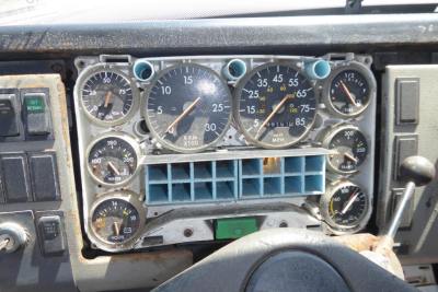 Dashboard of a Freightliner FL70 showing multiple gauges and controls in a weathered dash, including speedometer, tachometer, and auxiliary dials.