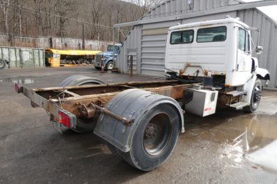 Flatbed chassis and cab of a Freightliner FL70 truck showing frame rails and rear dual wheels.