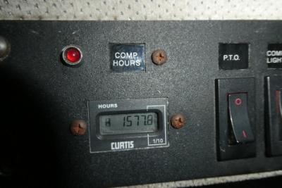 Panel with hour meter reading 15778 hours, labeled CURTIS, in-service control switches nearby (COMP HOURS, P.T.O.), part of a plow truck dashboard.