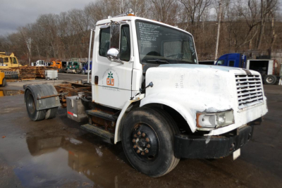 White Freightliner FL70 truck chassis with plow, partial branding on door, front bumper, and wheel wells visible.