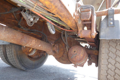 Truck undercarriage showing suspension and drivetrain components of a Freightliner FL70 plow truck.