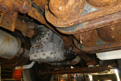 Freightliner FL70 drivetrain undercarriage showing rusty chassis, driveshaft, and transmission housing.