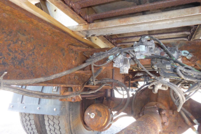 Freightliner FL70 chassis underside showing hoses, wiring, and rusty drivetrain components with dual rear wheels.