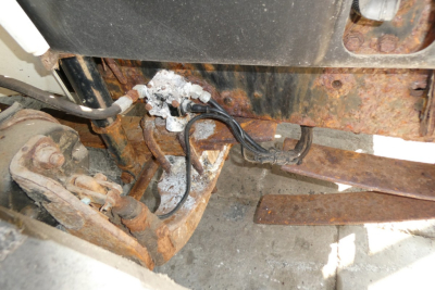 Truck chassis showing exposed wiring harness and rusty frame with hydraulic lines and plow mounting area.