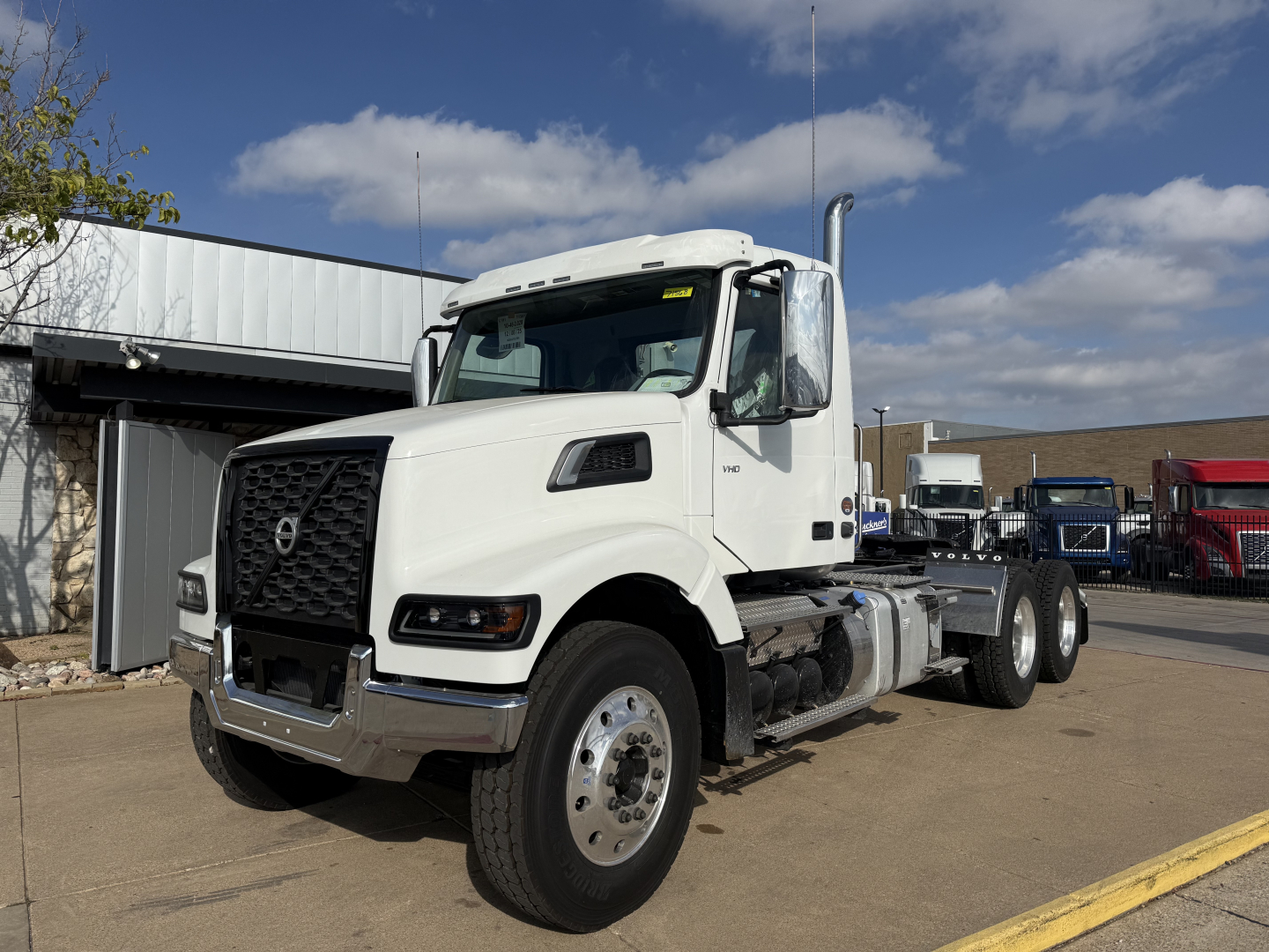 Volvo VHD64FT300 conventional daycab truck, white cab, three-axle configuration, front grille with Volvo logo, large side mirrors, fuel tanks, and chassis rails visible.