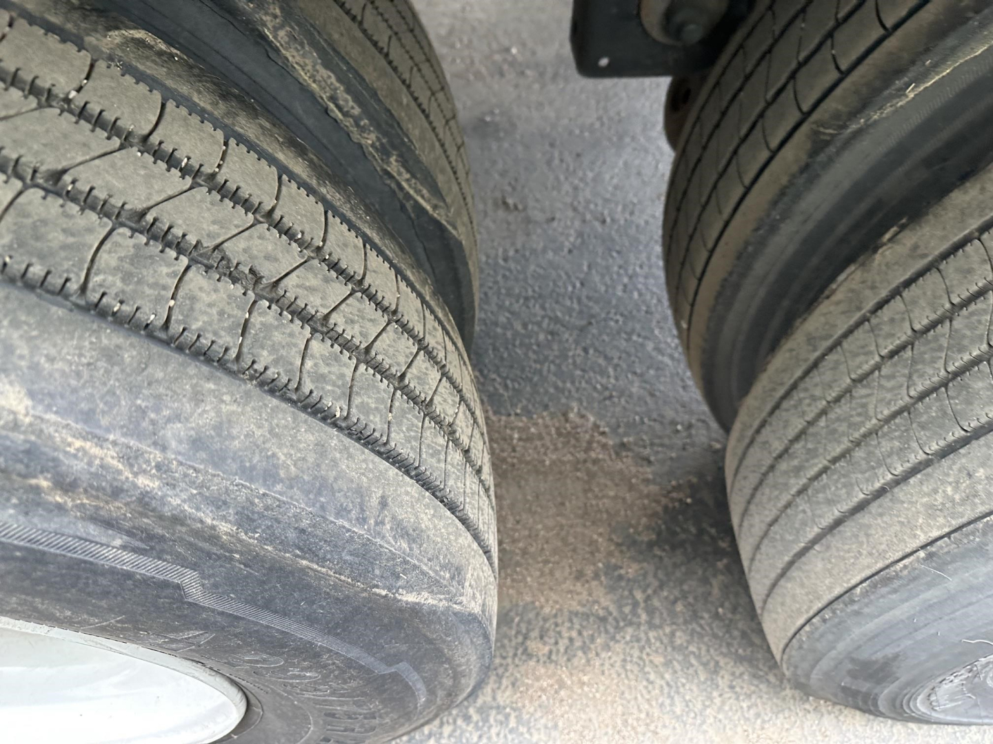 Dual trailer tires and mud between wheels, portion of trailer undercarriage visible.