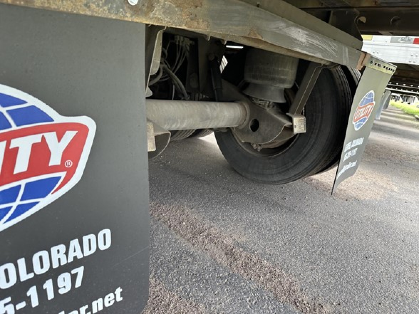 Trailer undercarriage showing drivetrain components, axle, suspension, and mudflap with Colorado contact details in partial view.