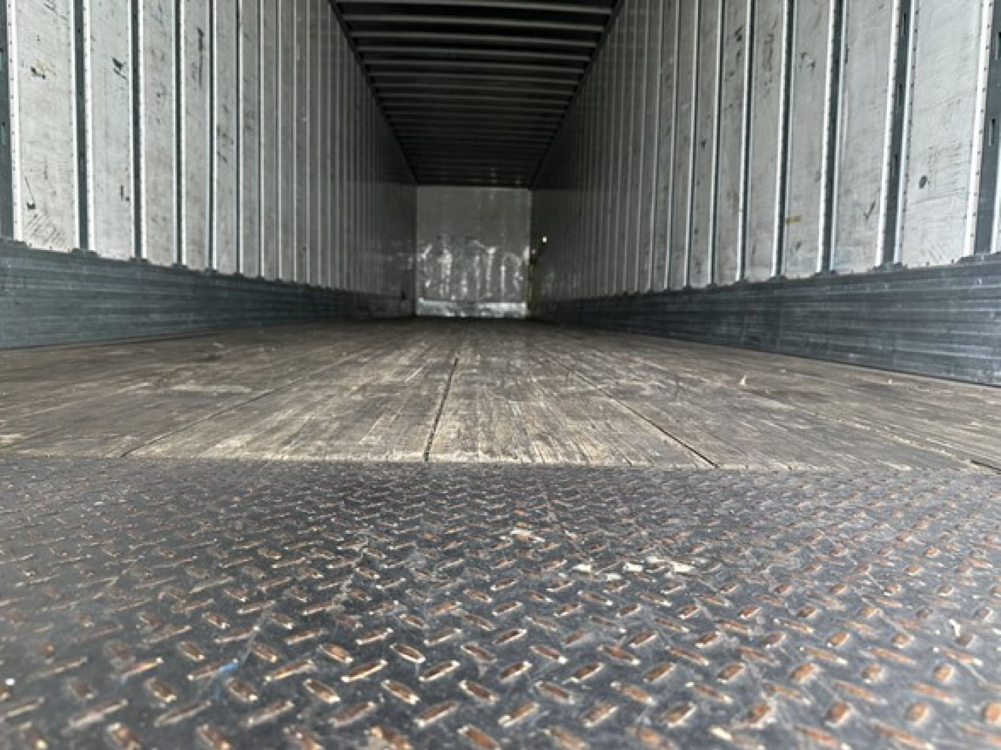 Utility trailer interior showing empty cargo space with metal walls and diamond tread steel floor.